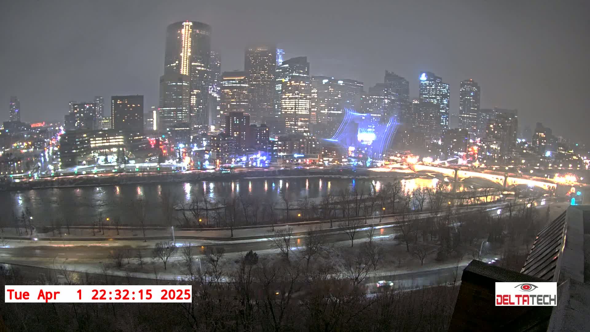A nighttime view of a snow-covered city skyline illuminated by lights across a river.