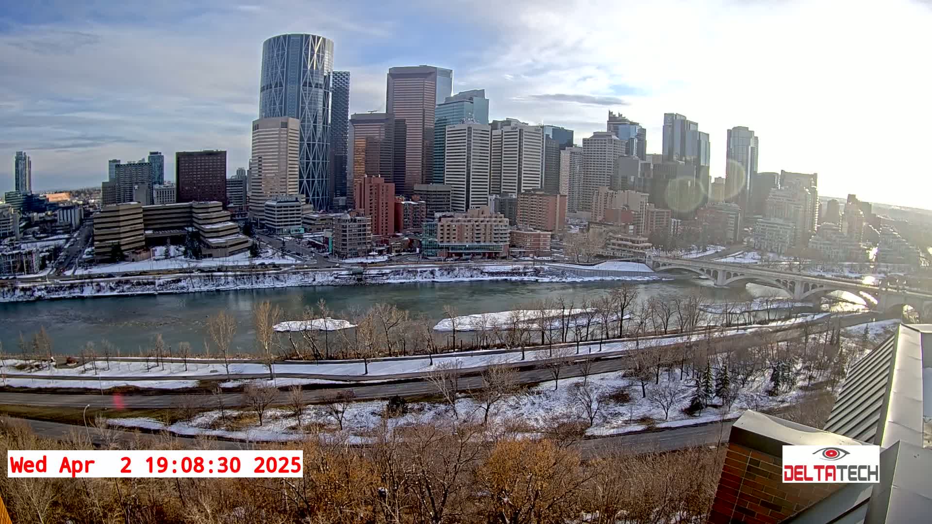 A city skyline with numerous skyscrapers is visible across a snow-covered river under a partly sunny sky.