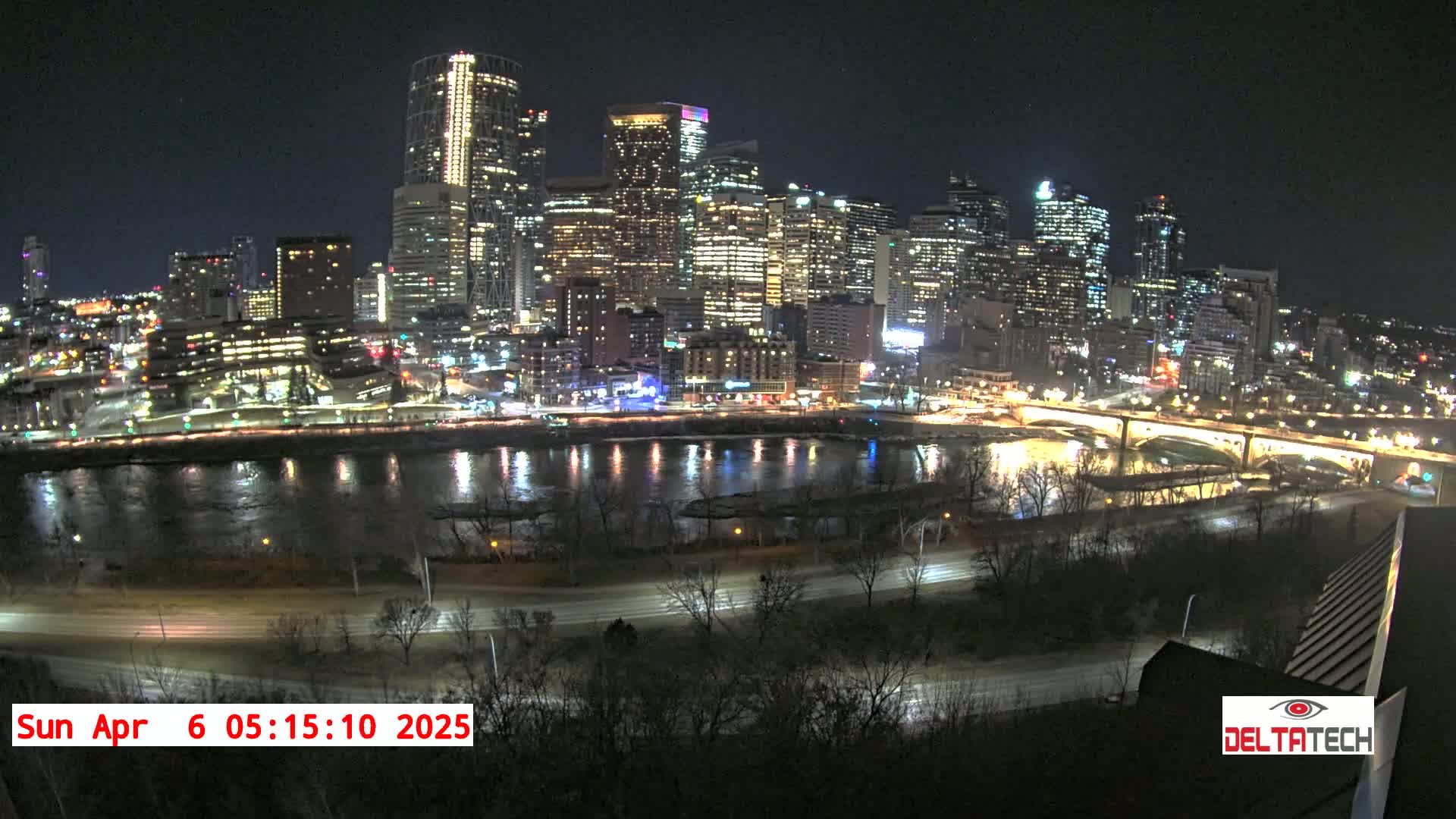 A nighttime cityscape with a river reflecting the city lights, under a clear sky.