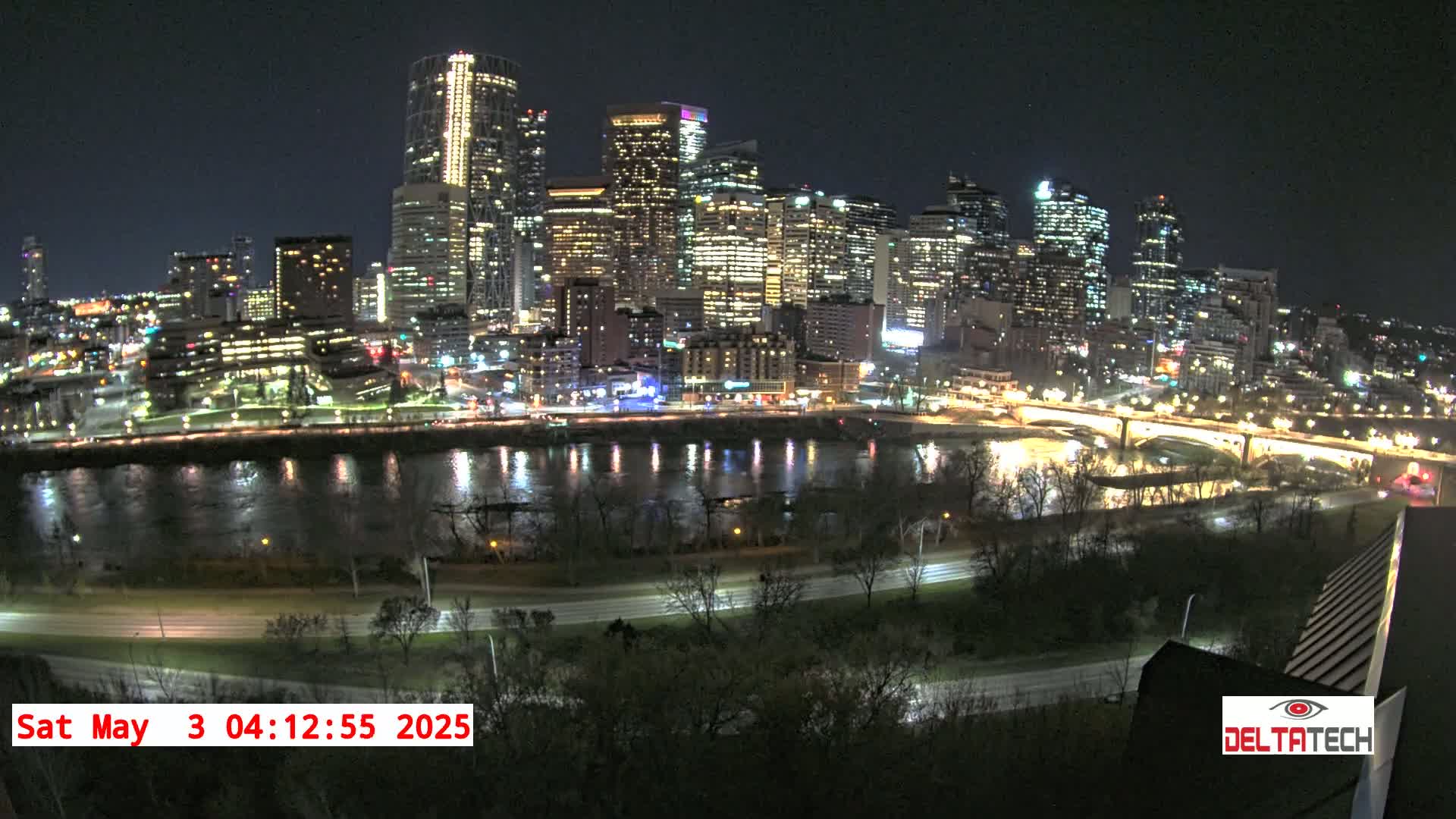 A nighttime cityscape with a river reflecting city lights under a clear sky.
