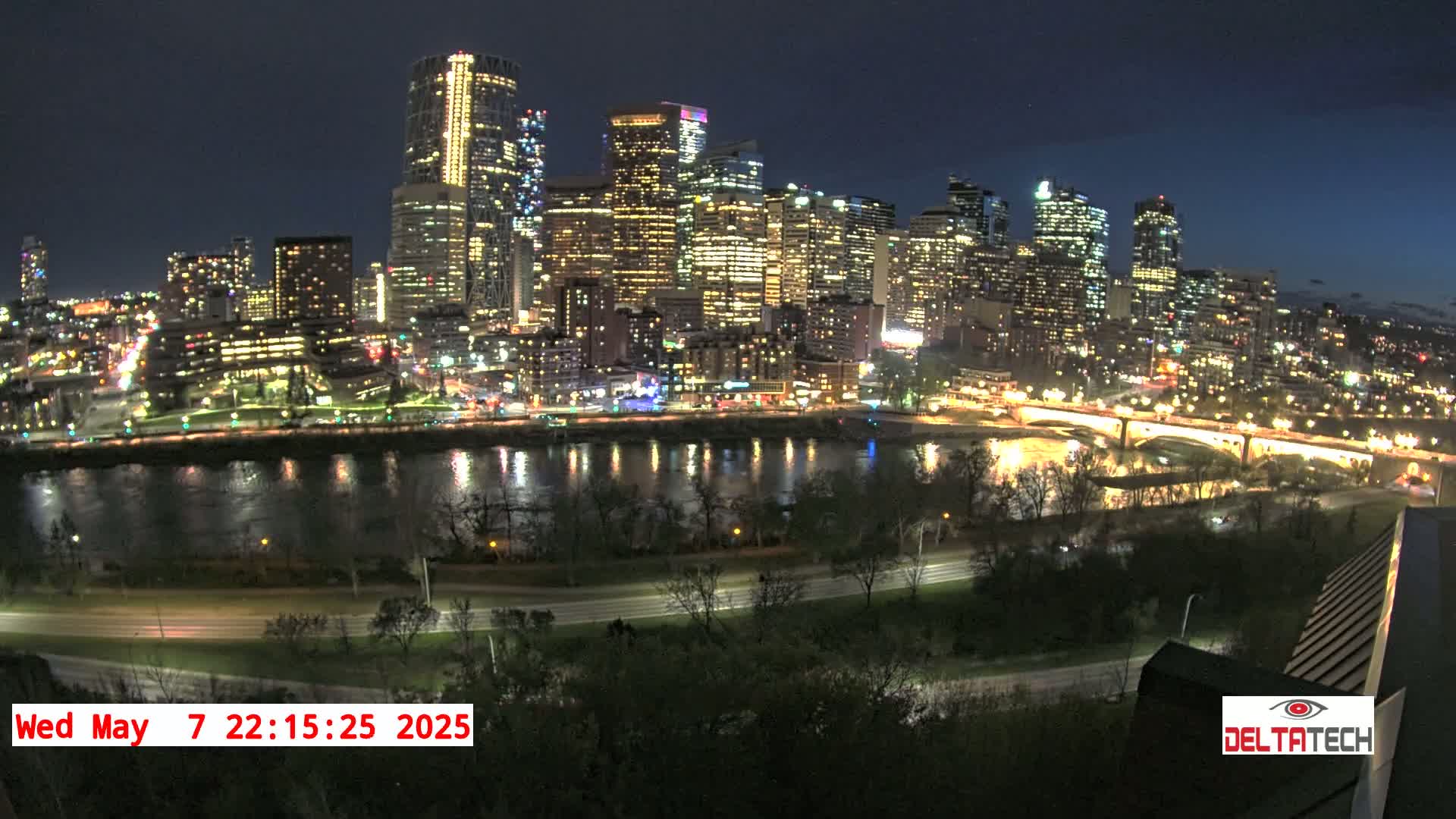 A nighttime cityscape with brightly lit skyscrapers and a river reflecting the city lights under a clear sky.