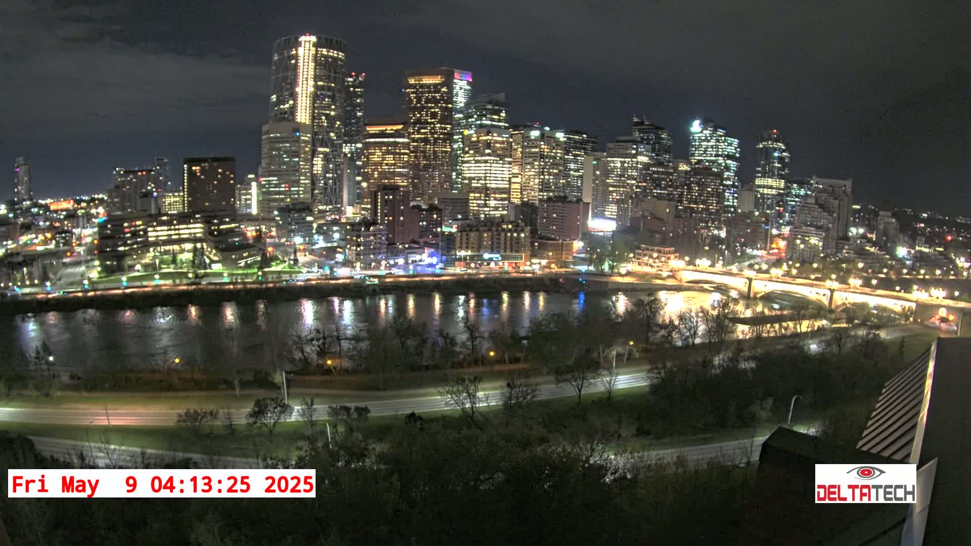 A nighttime cityscape with a river reflecting the city lights under a mostly clear sky.