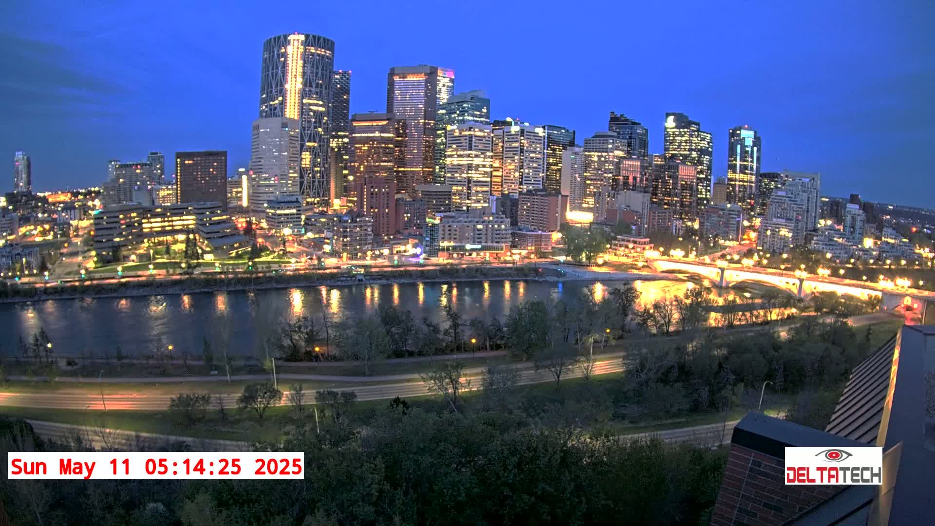 A city skyline illuminated at night, with a river reflecting the city lights in the foreground under a twilight sky.