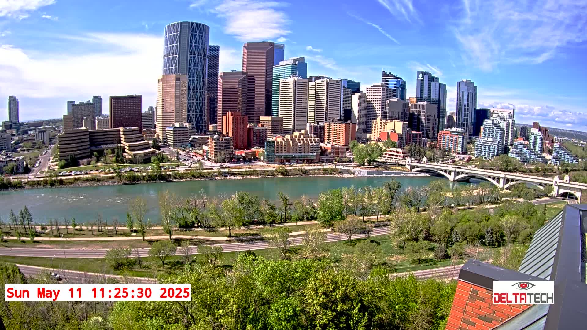 A cityscape with many tall buildings sits on the far side of a wide, calm river under a sunny sky.
