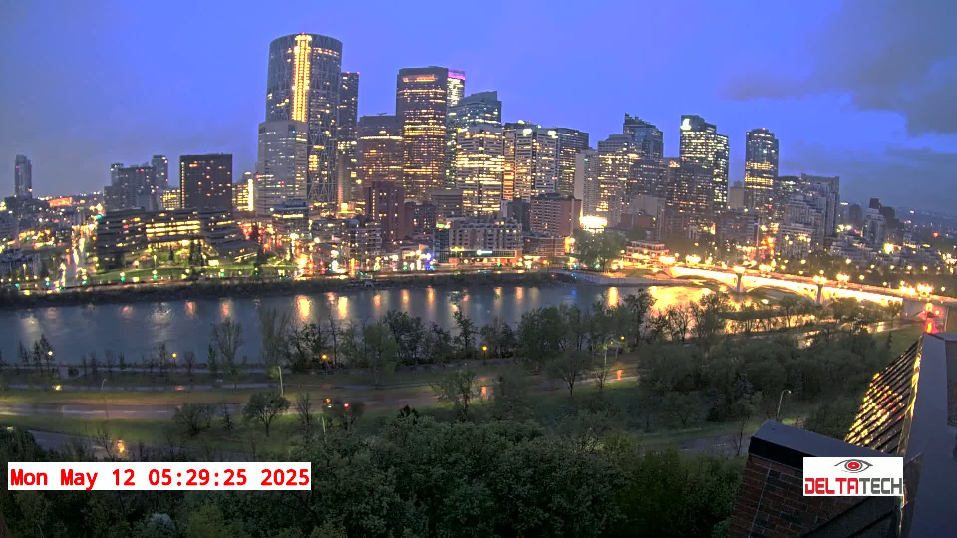 A nighttime cityscape with illuminated skyscrapers across a river, under a partly cloudy sky.