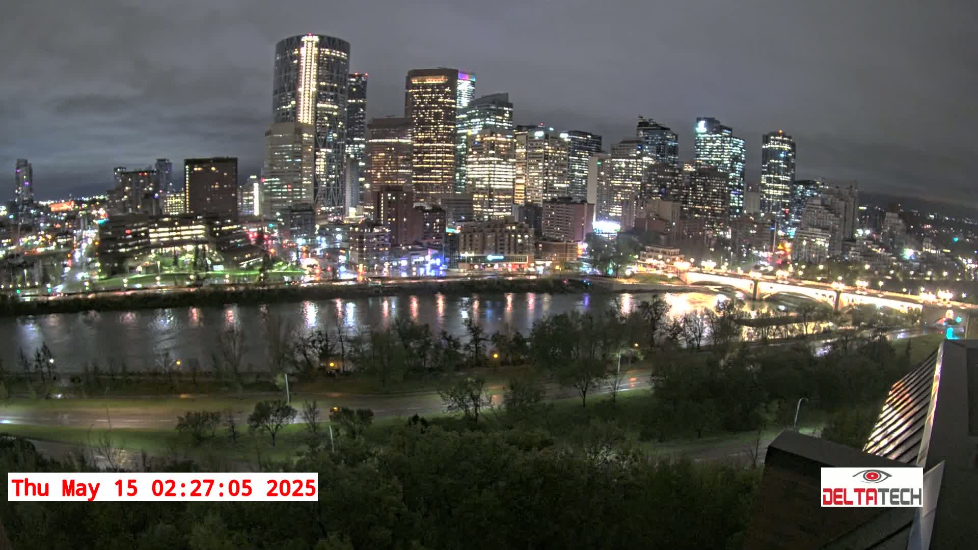 A nighttime view of a city skyline across a river, under a cloudy sky.