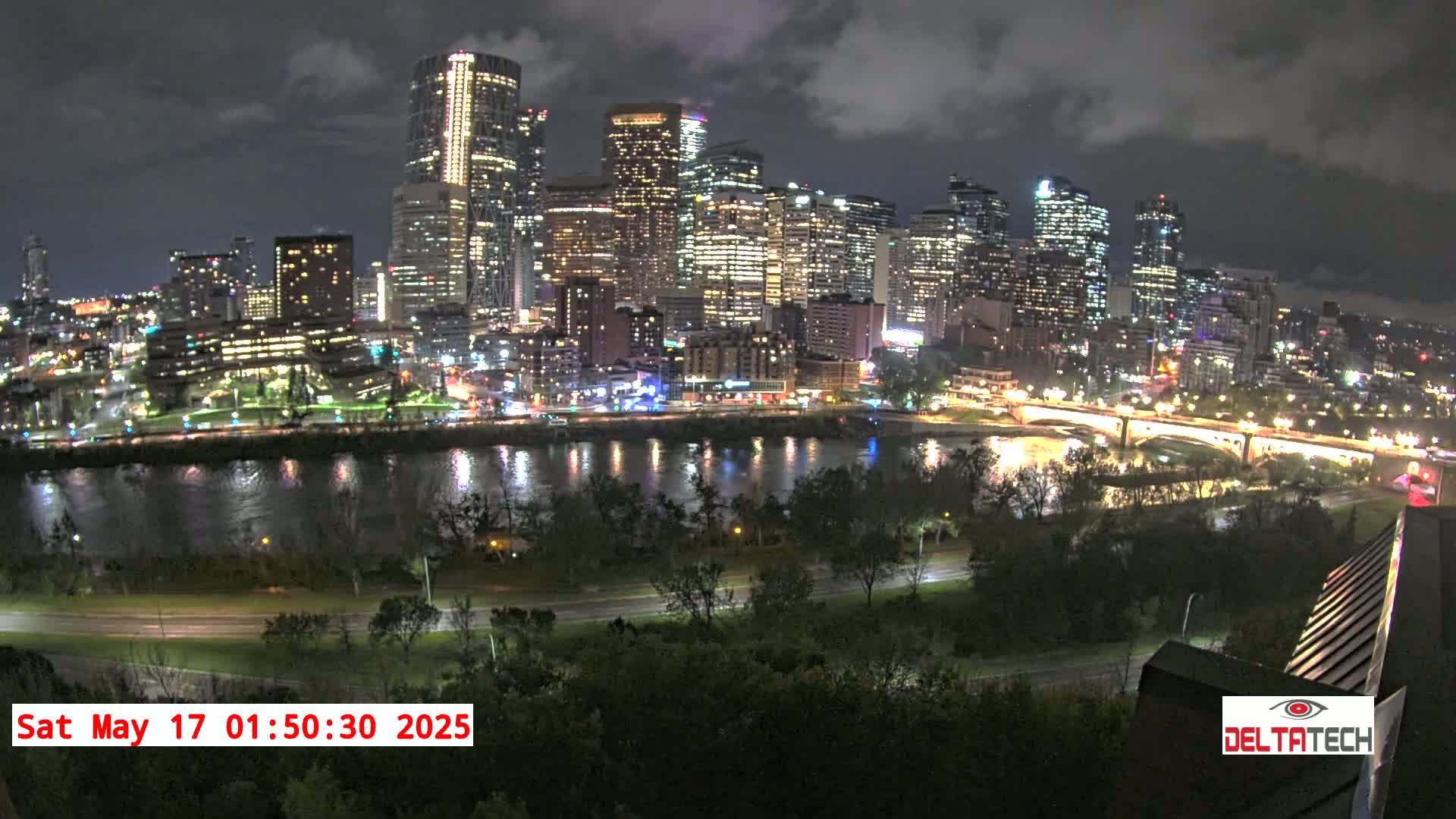 A nighttime view of a city skyline illuminated with lights across a river, under a cloudy sky.