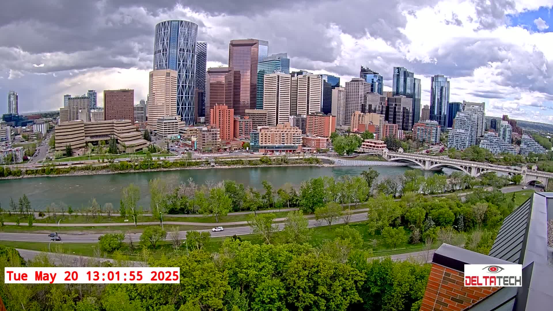 A city skyline with numerous high-rise buildings is seen across a river under a partly cloudy sky.