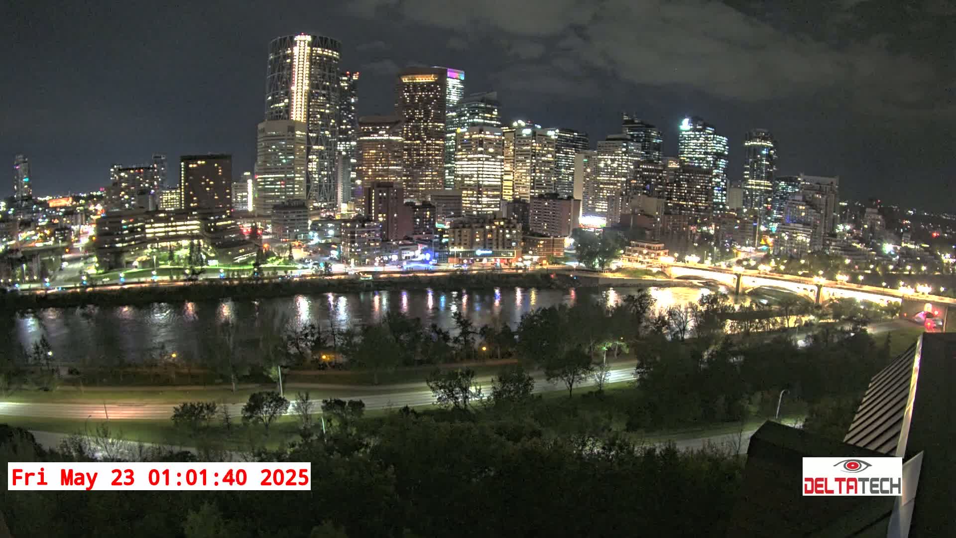A nighttime cityscape with a river reflecting the city lights, under a partly cloudy sky.