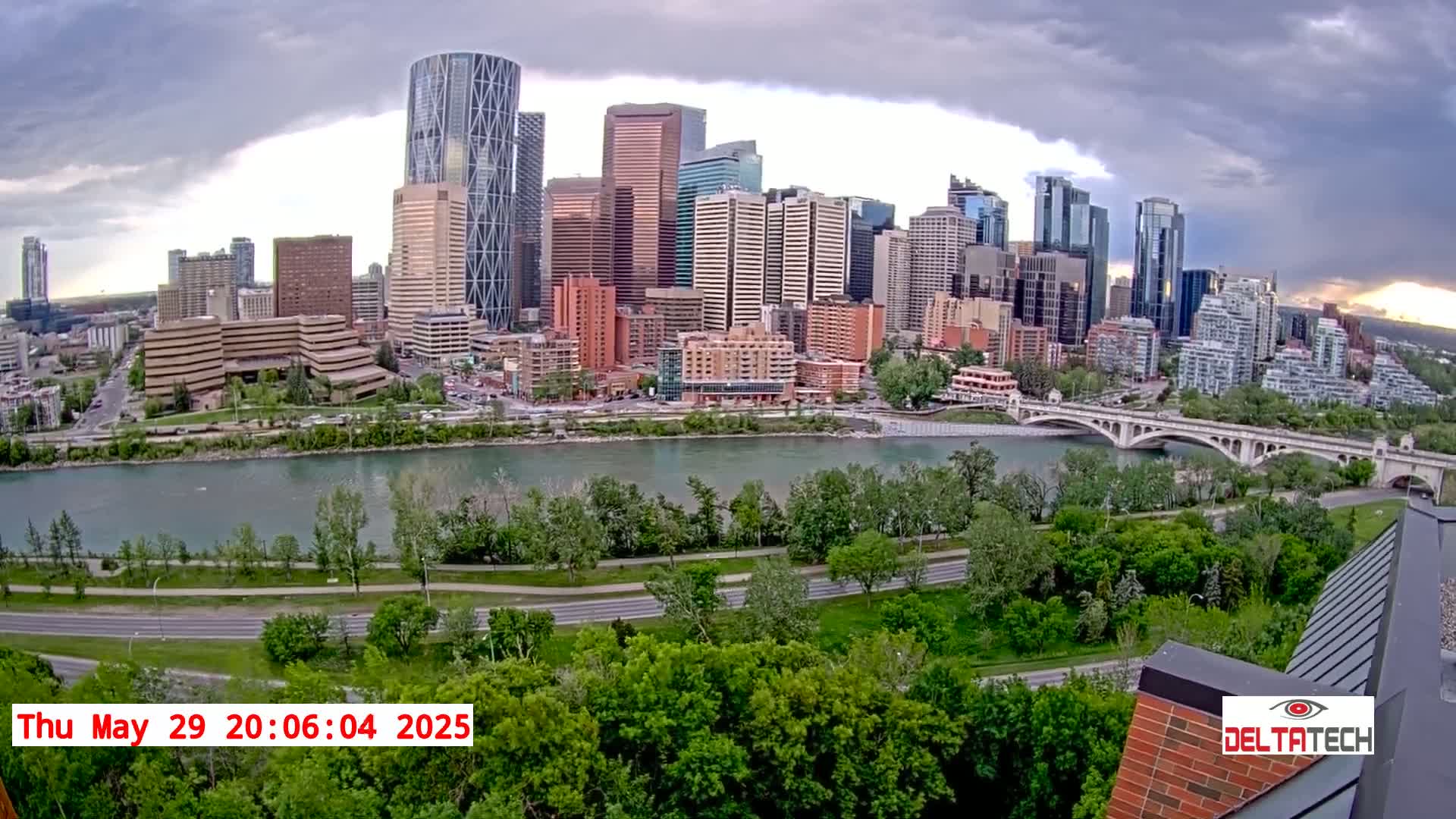 A cityscape with many skyscrapers is seen across a river under a cloudy sky.