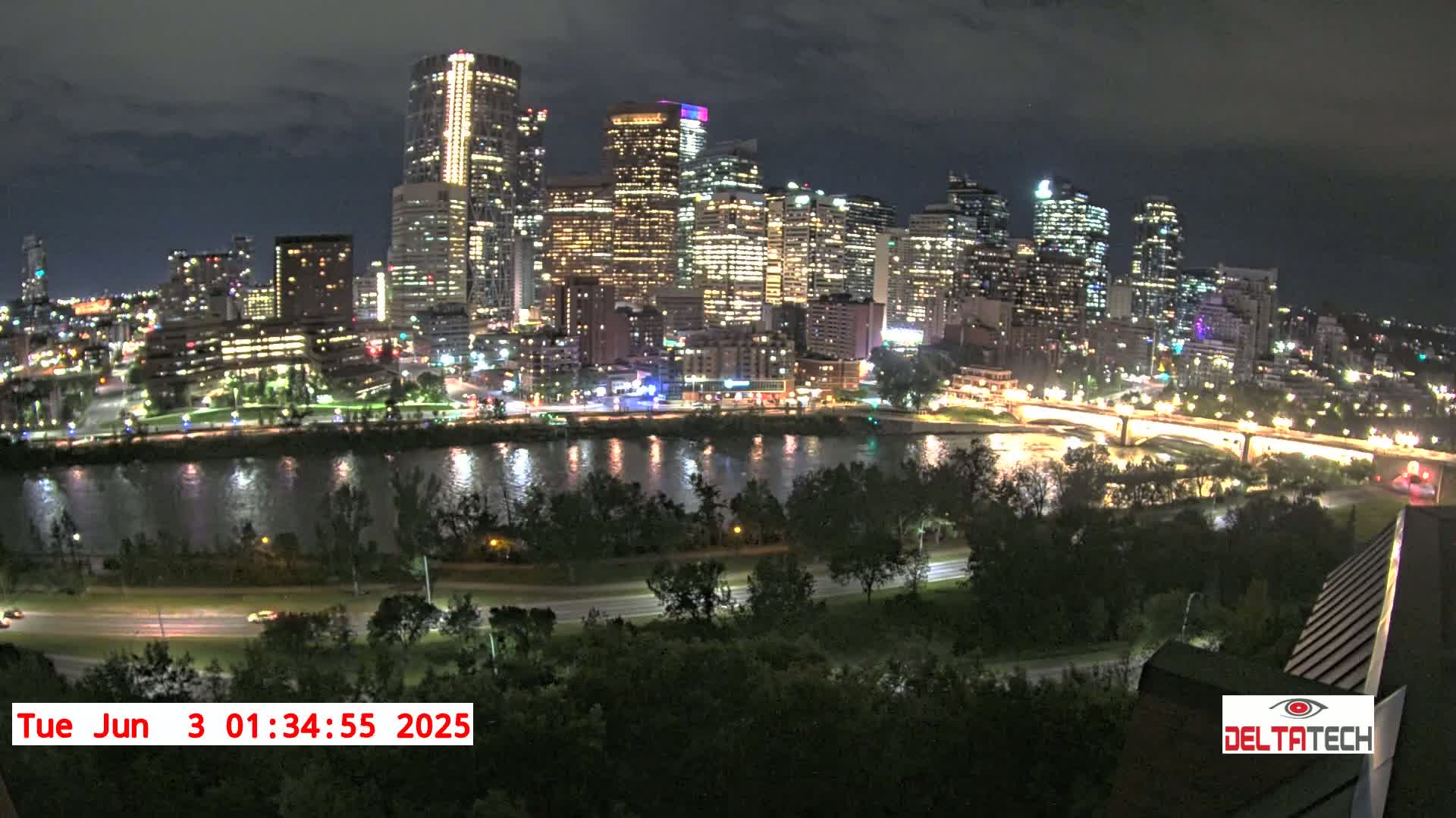 A nighttime view of a city skyline across a river, with lights illuminating the buildings and roads.