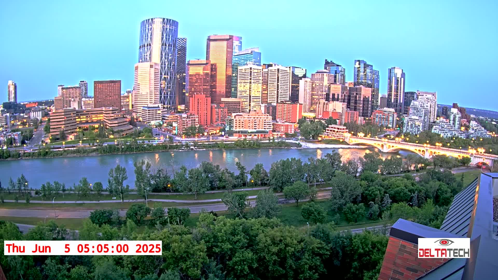 A city skyline with numerous skyscrapers and high-rise buildings is situated along a river at dawn, with a bridge visible in the foreground.