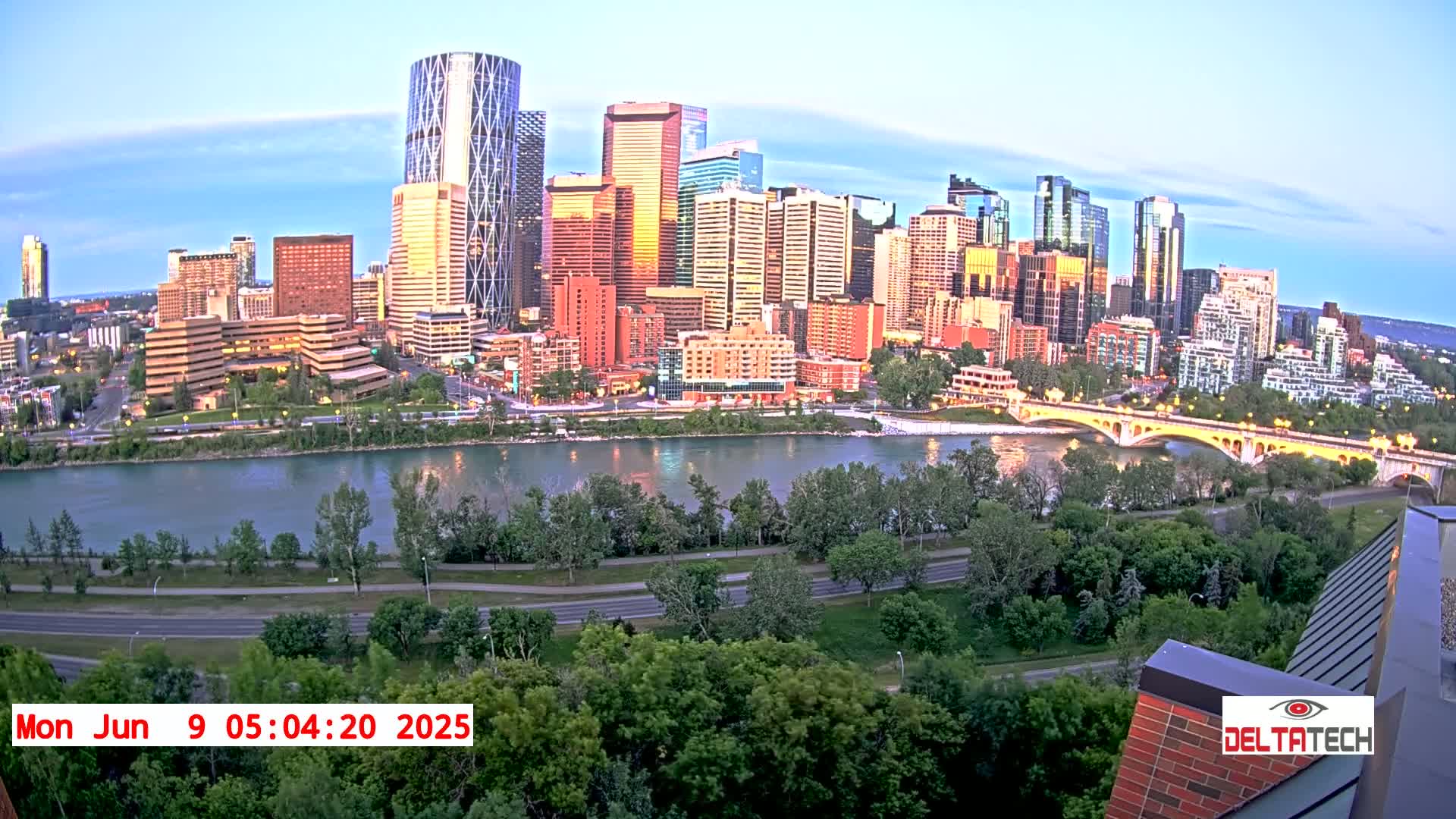 A city skyline with many tall buildings sits on the far bank of a wide river under a twilight sky.