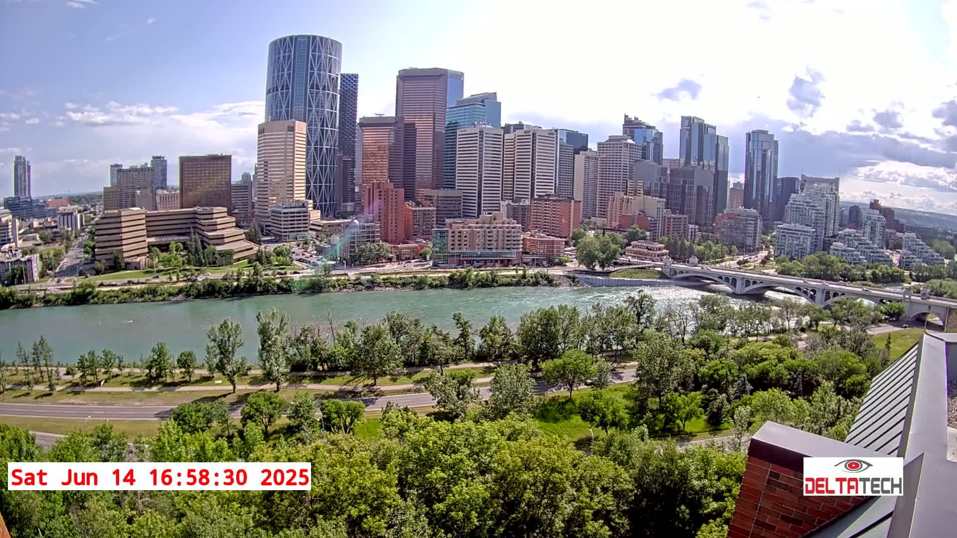 A city skyline with numerous skyscrapers is seen across a river on a partly cloudy, sunny day.