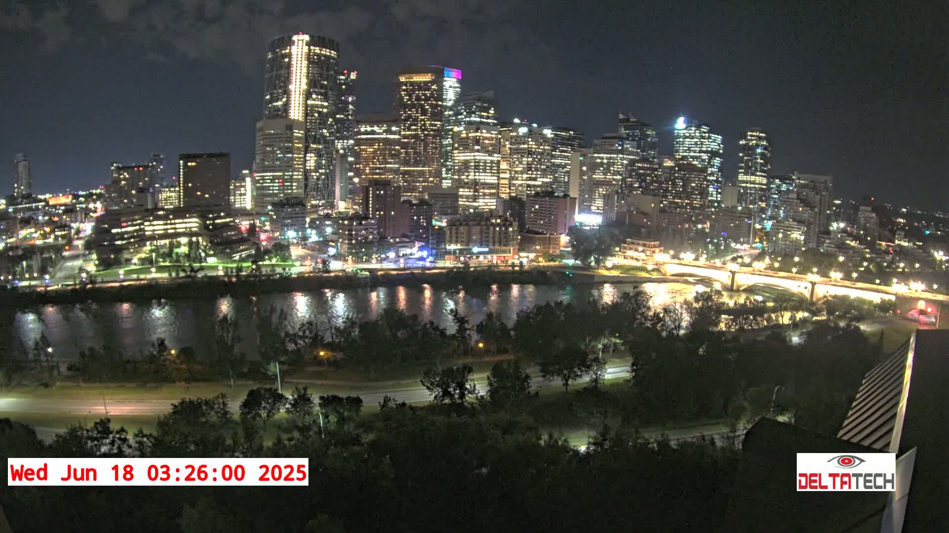 A nighttime view of a city skyline across a river, under a mostly clear sky.