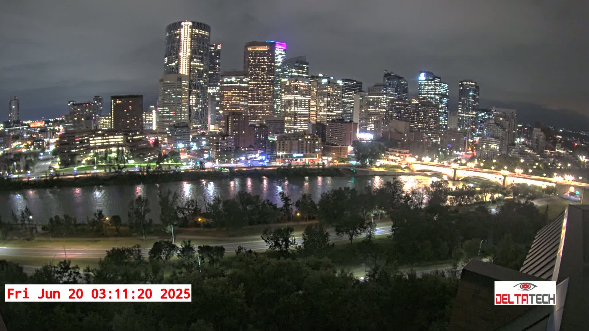 A nighttime view of a city skyline illuminated with lights across a calm river, under an overcast sky.