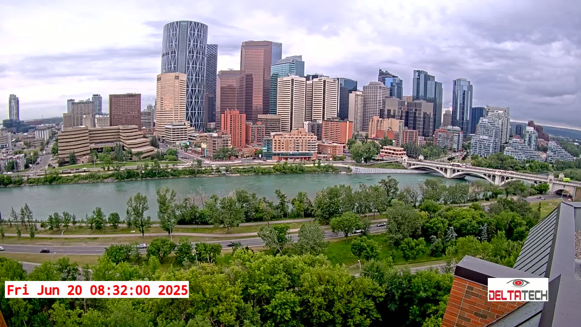 A city skyline with numerous skyscrapers is seen across a river, under a partly cloudy sky.