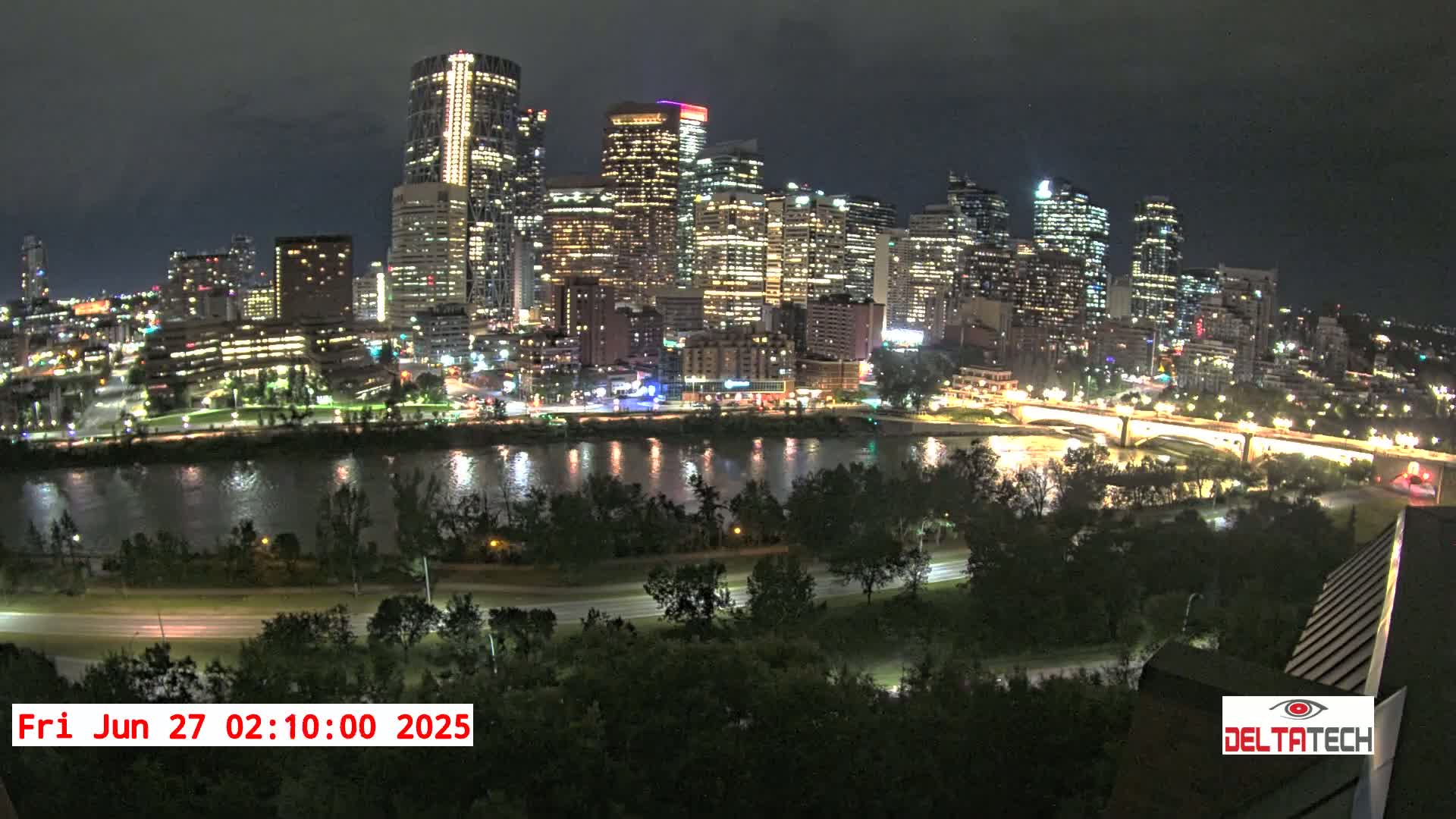 A nighttime view of a city skyline illuminated across a river, under a dark sky.