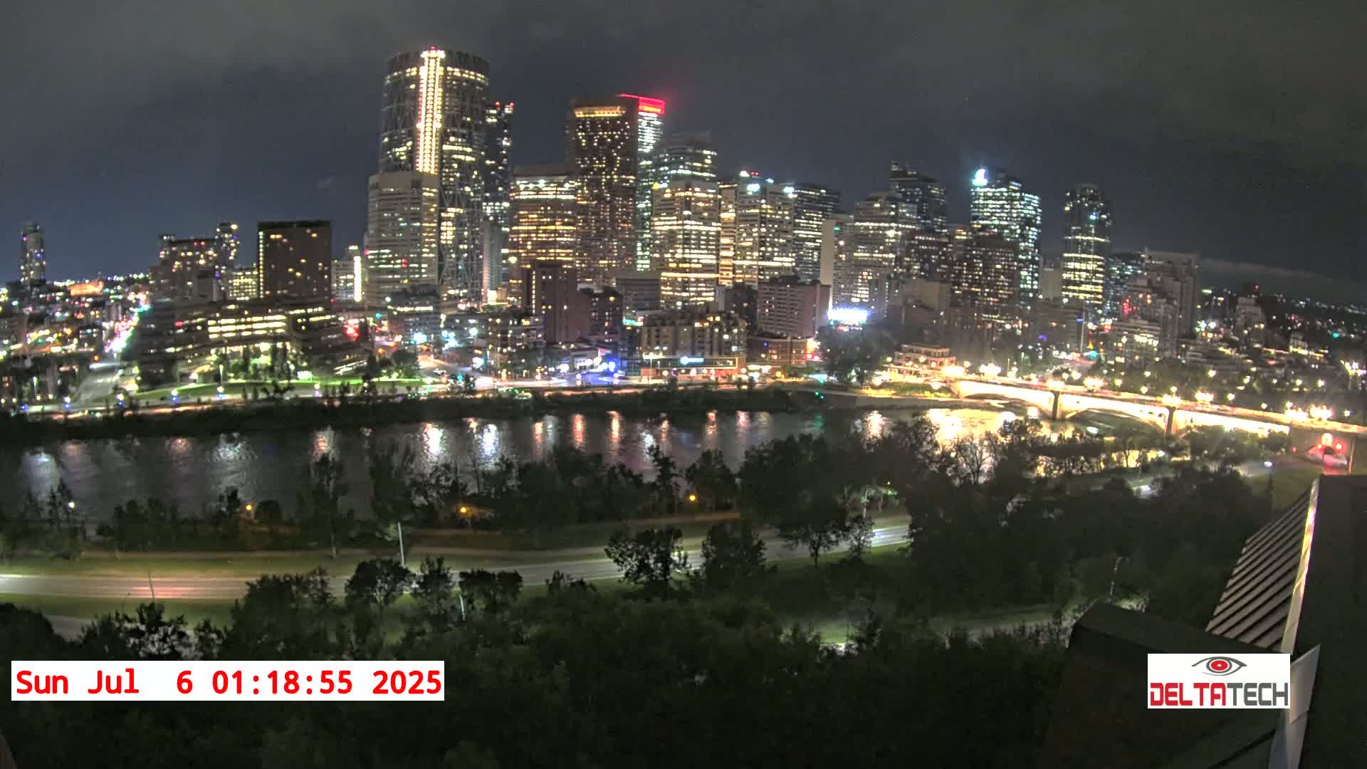 A nighttime view of a city skyline illuminated with lights across a river, under a cloudy sky.