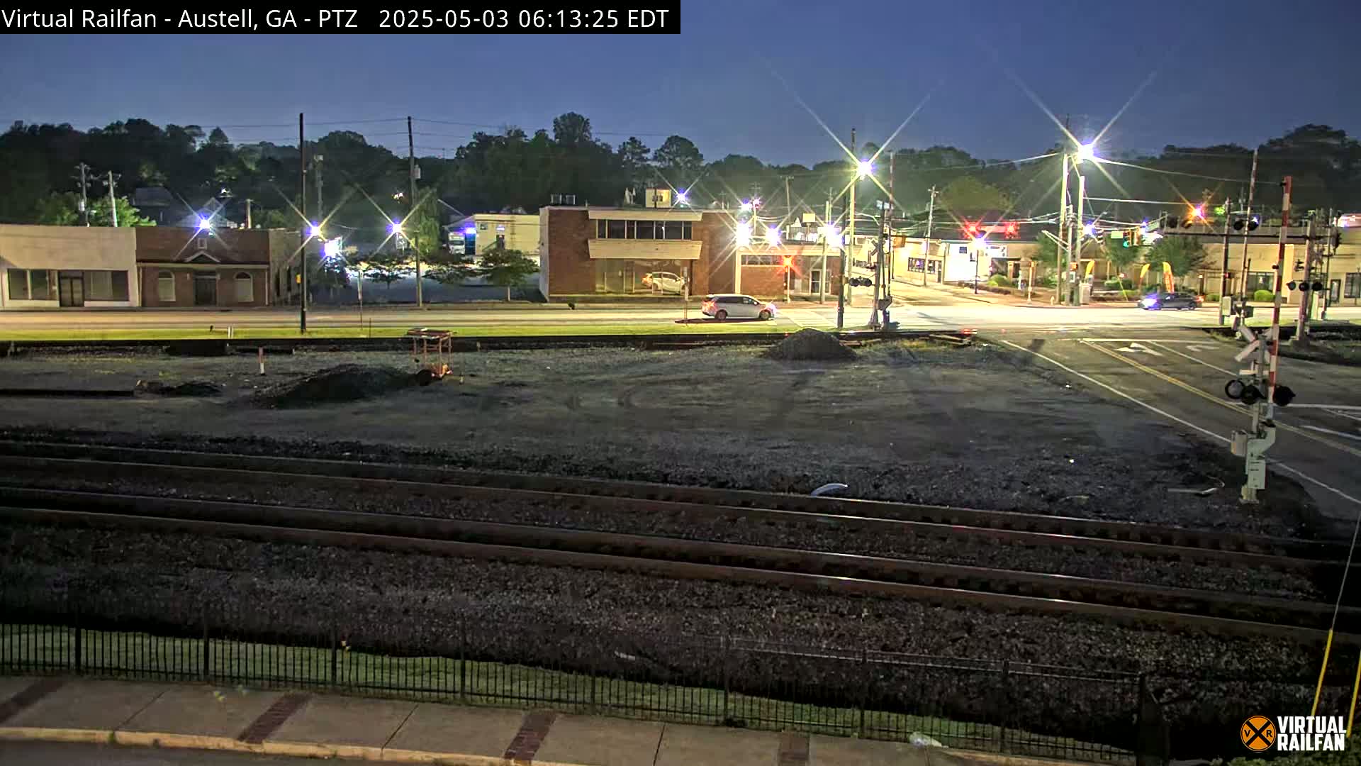 A nighttime view of a street intersection with train tracks in the foreground, under clear skies.
