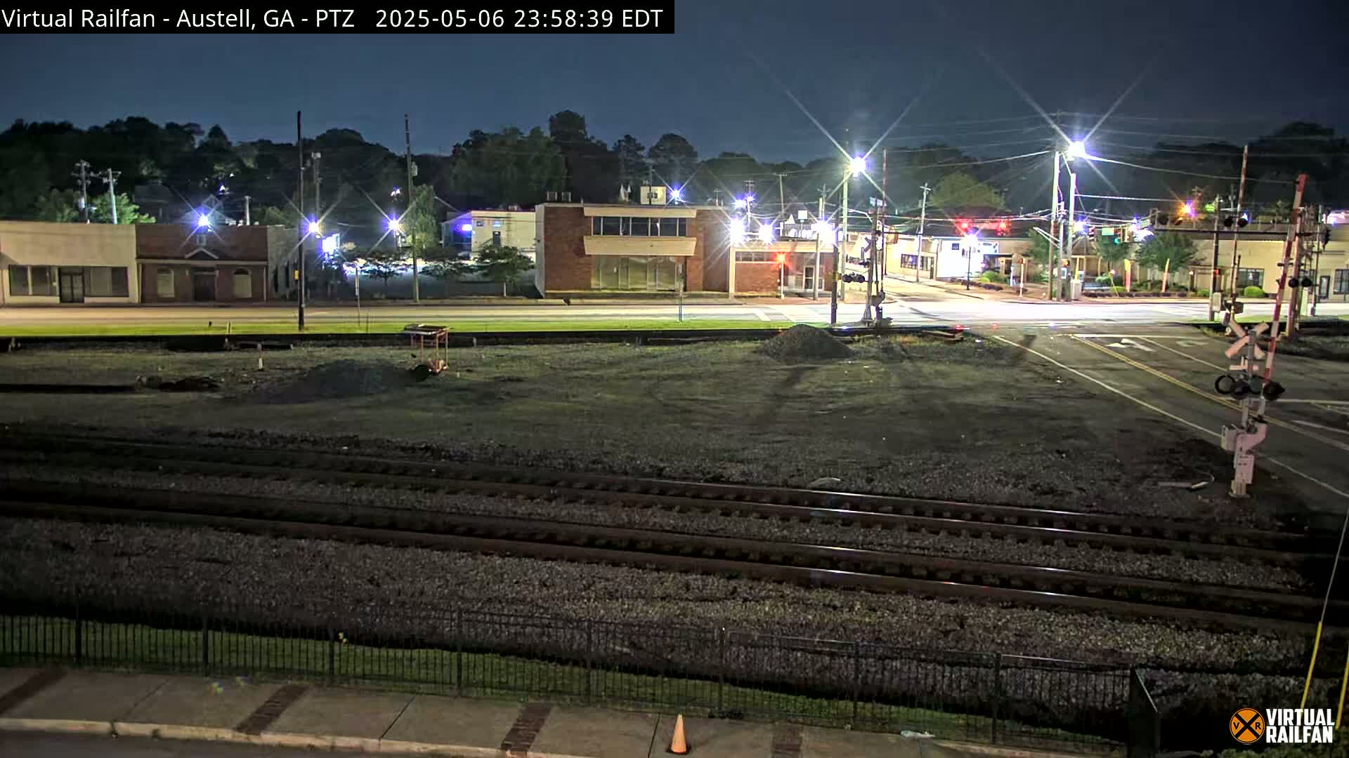 A nighttime view of a street intersection with buildings and train tracks, under a clear sky.