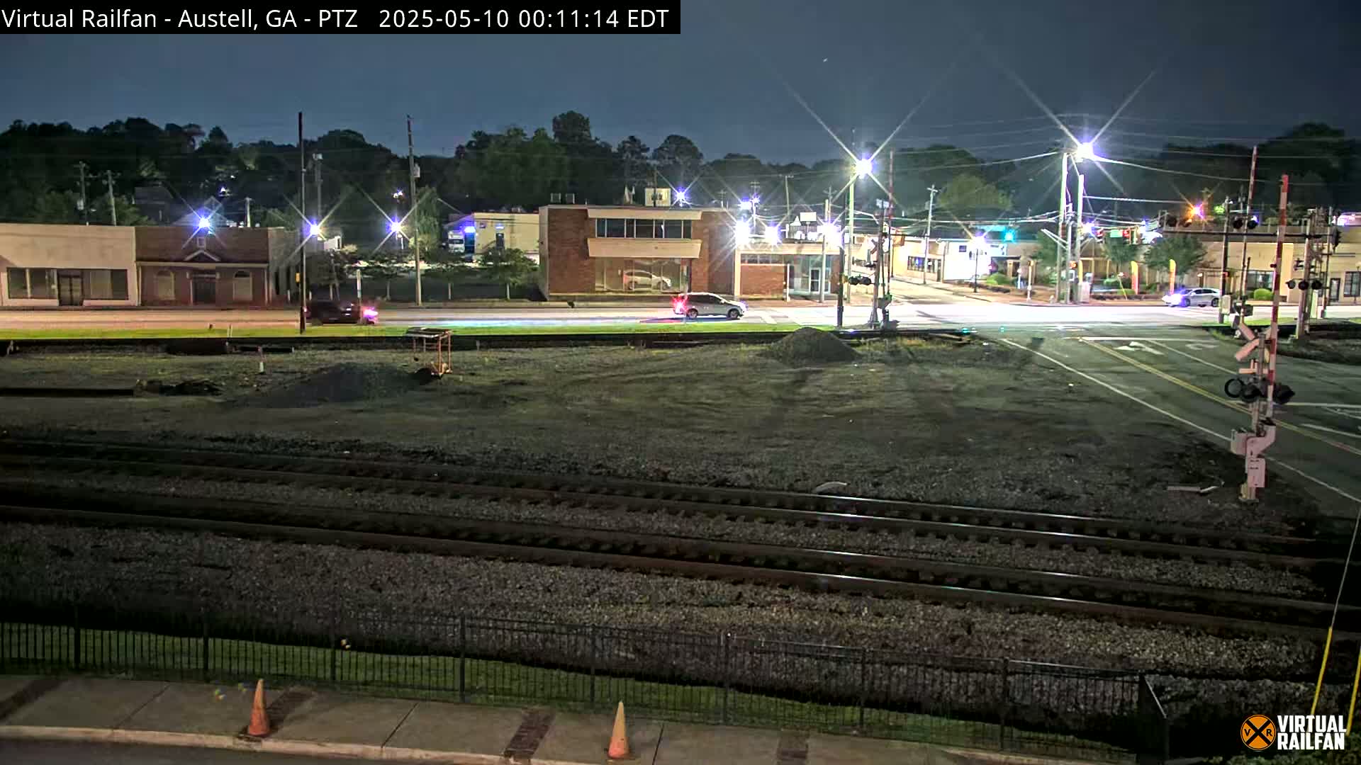 A nighttime view of a street intersection near railroad tracks, with several cars visible and streetlights illuminating the scene.