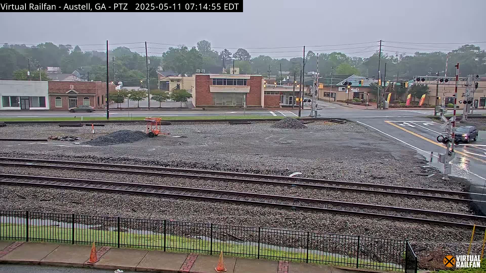 A wet, overcast day shows a view of railroad tracks, a street intersection, and some buildings in the distance.