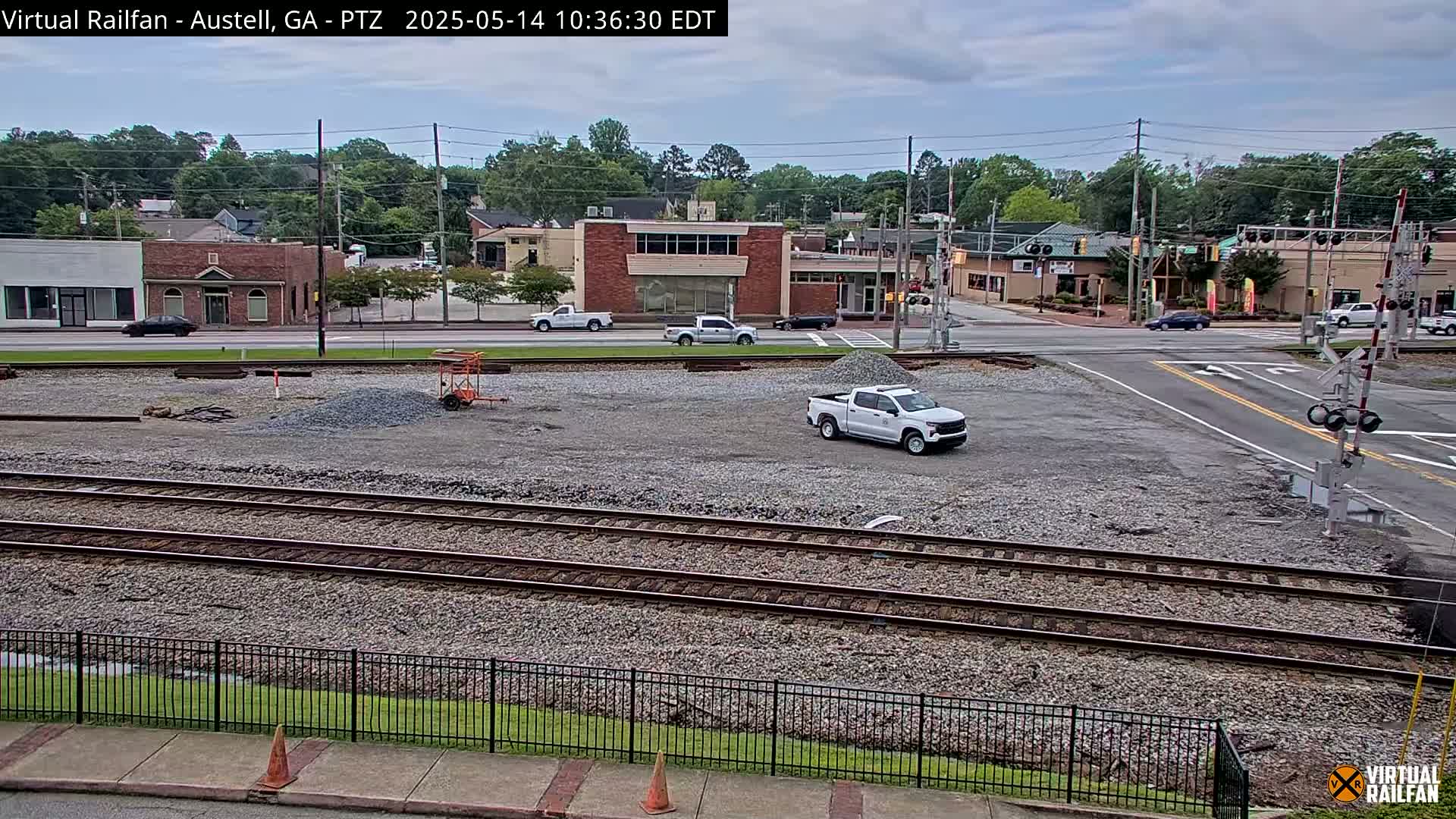 A mostly sunny day reveals a view of railroad tracks and a construction site next to a street intersection with several buildings and vehicles.