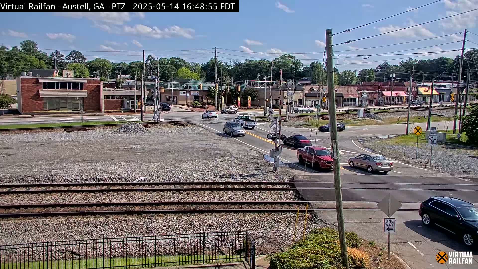 Several cars are driving through a town intersection near railroad tracks on a sunny day.
