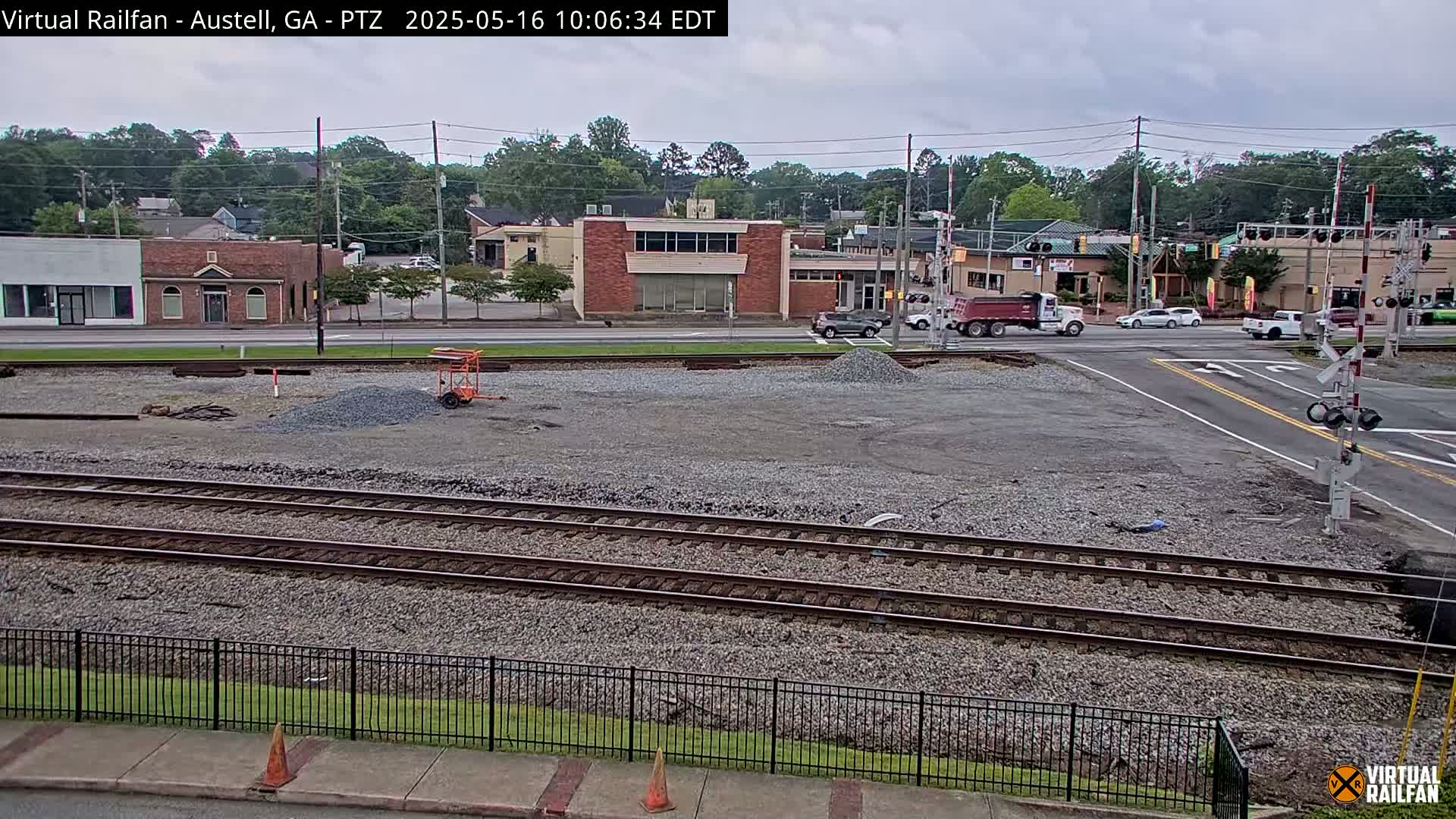 A view of railroad tracks in a mostly overcast urban setting, with construction materials and several vehicles visible in the background.