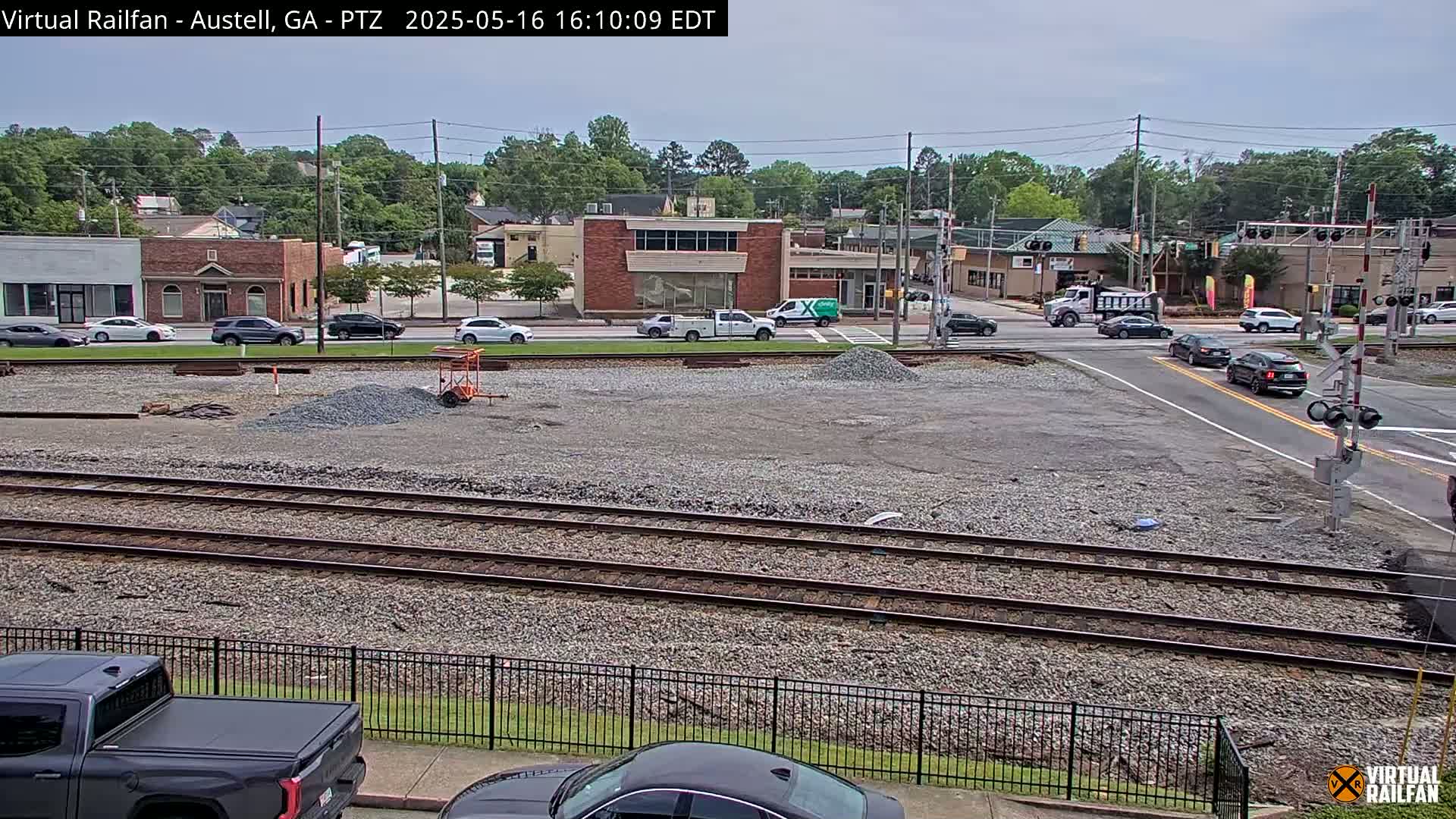 A mostly clear day reveals a street intersection near some railroad tracks, with several vehicles on the road and piles of gravel in a construction zone.