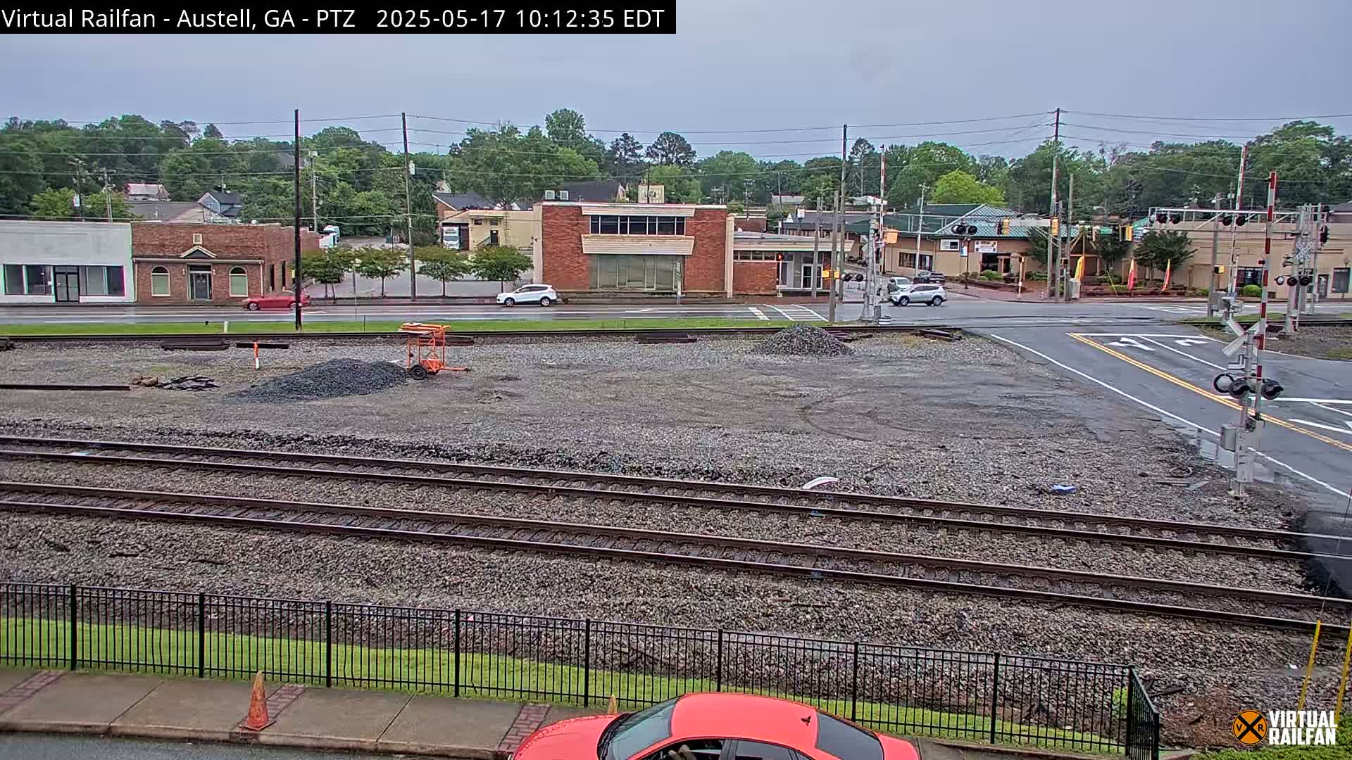 A view of railroad tracks in a town on an overcast day, with several buildings and cars visible in the background.