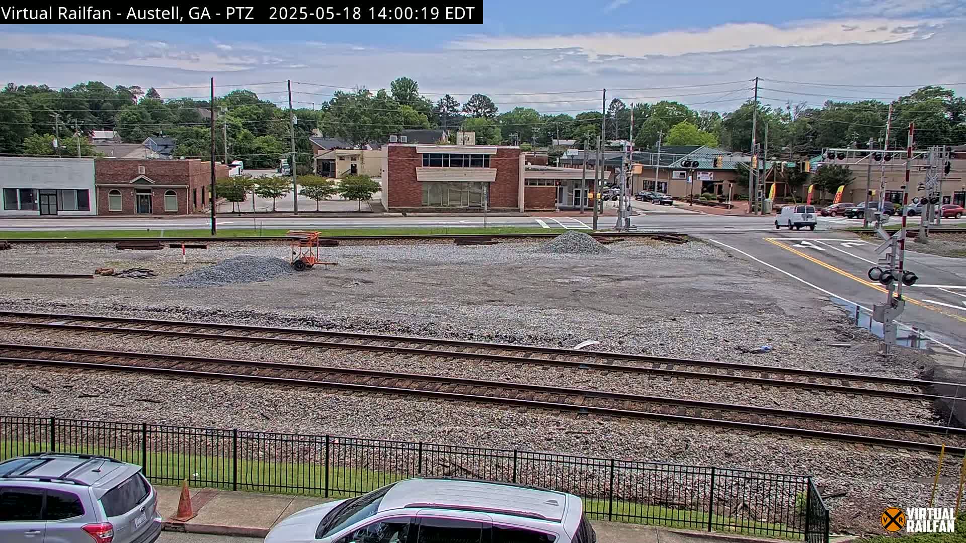 A mostly clear day shows a railroad crossing near a town's main street with some construction underway in the foreground.