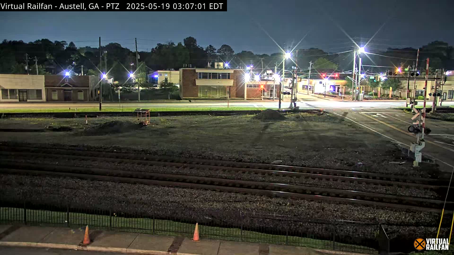 A nighttime view of a train crossing in a town, with several buildings visible in the background under a clear, dark sky.