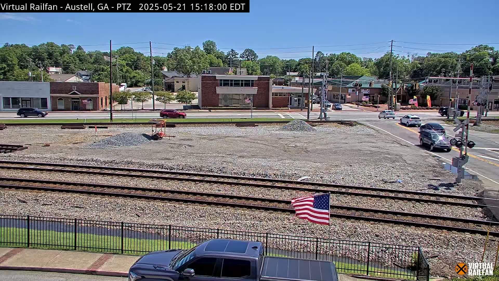 A sunny view of a small town's streets and railroad tracks with several cars and an American flag.