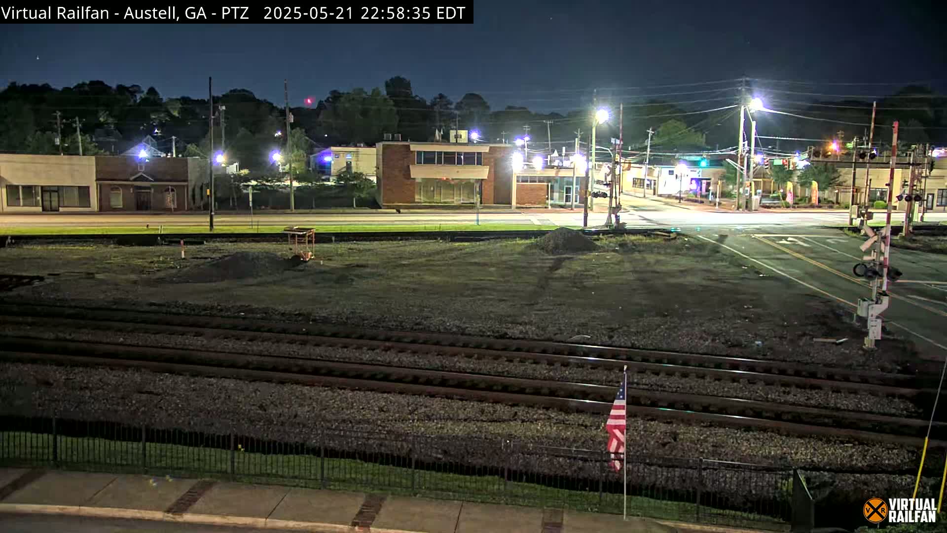A nighttime view of a train track next to a street with buildings under a clear sky.