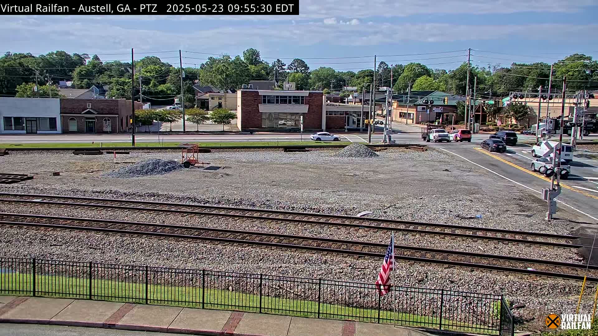 A sunny view of a railway crossing next to a town's main street, where construction is underway on a plot of land.