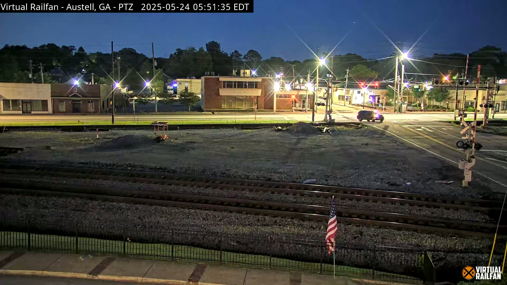 A nighttime view of a street intersection with a vehicle and railroad tracks, under a clear, dark sky.