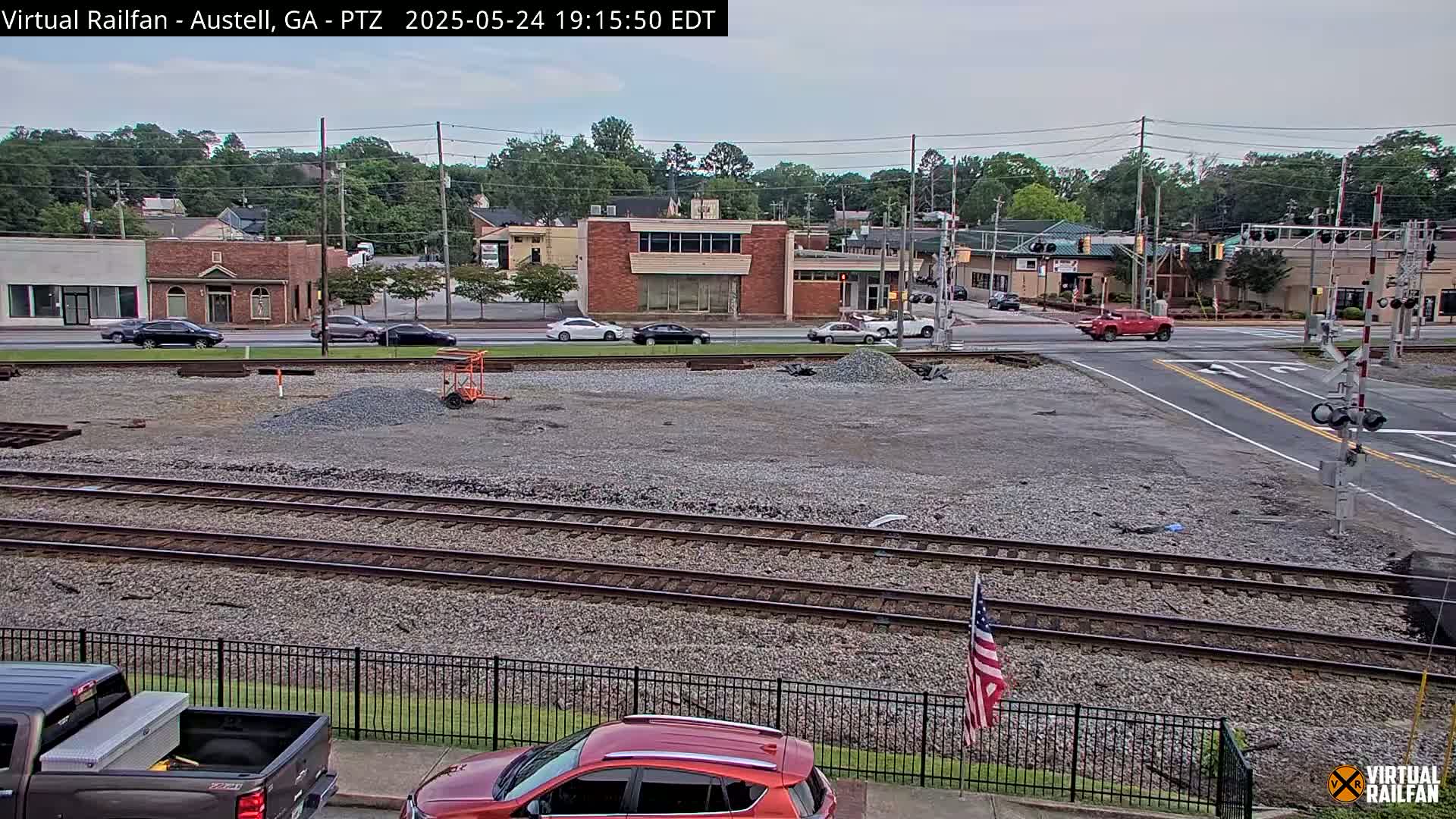 A view of a town's railway crossing under a partly cloudy sky, with construction materials and vehicles present.