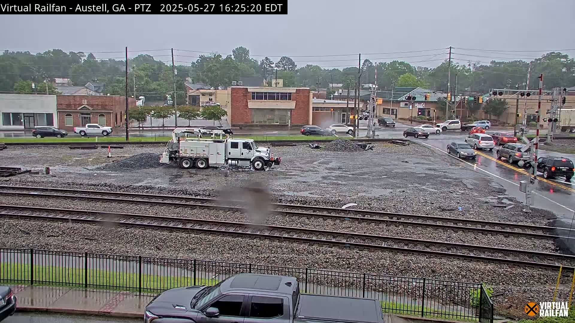 A work truck is parked near a pile of gravel beside train tracks in a rainy town.