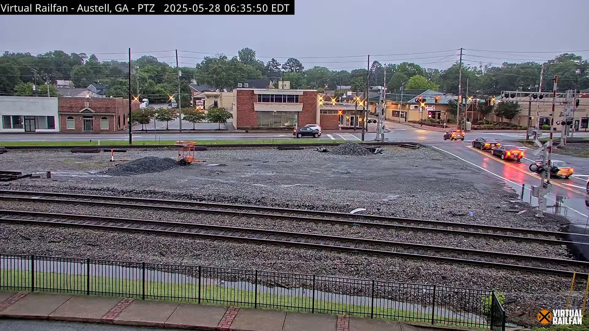 A wet, overcast day reveals railroad tracks in front of a small town's buildings and a street intersection with several cars.