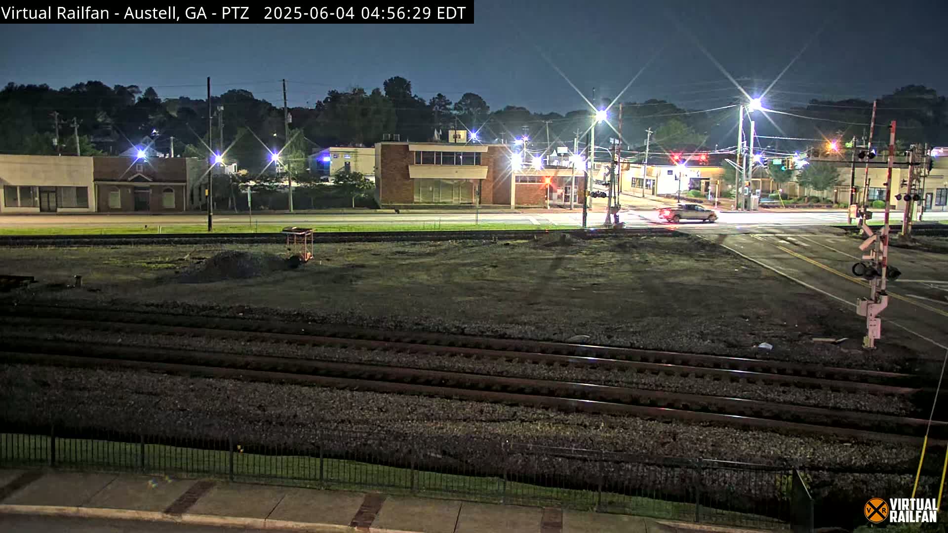 At night, a train track divides a street intersection with buildings and streetlights visible in the background.