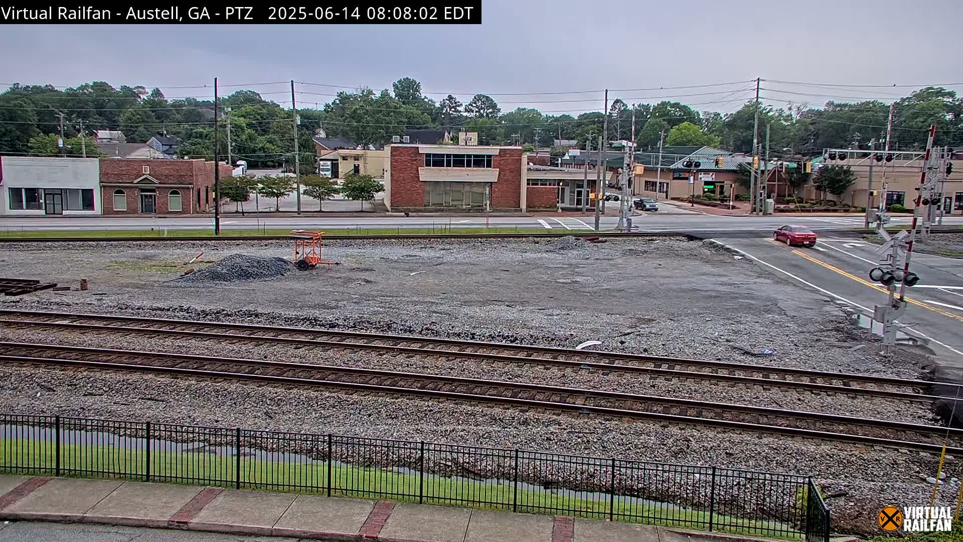 A mostly clear day shows a view of railroad tracks next to a street with buildings and a few cars, with some construction visible.