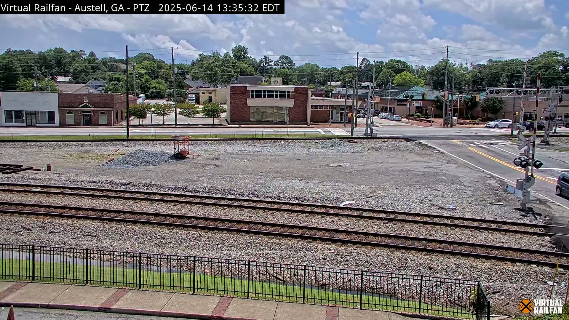 A mostly clear day reveals a view of railroad tracks in front of a small town's buildings and a road intersection with railroad crossing gates.