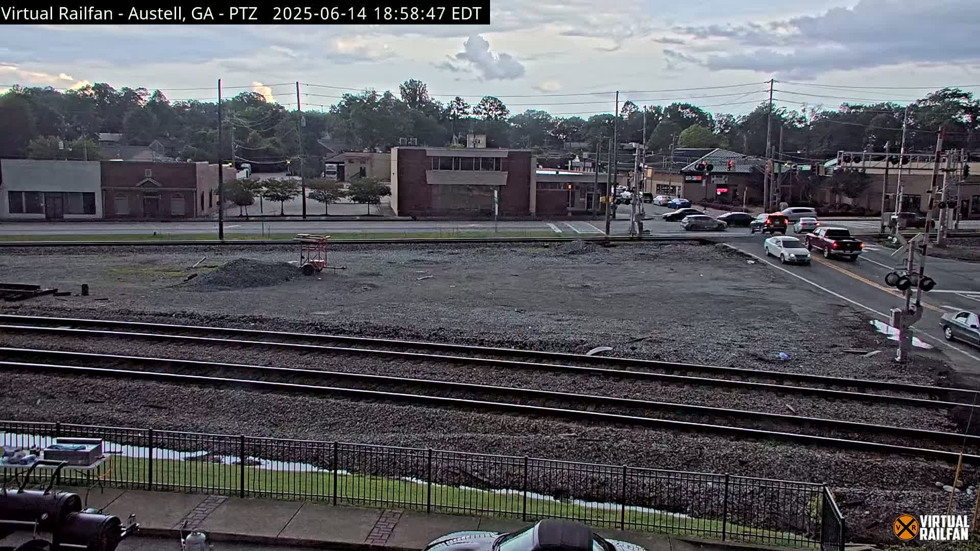 A mostly clear day reveals a view of railroad tracks in front of a small town's buildings and a road intersection with railroad crossing gates.
