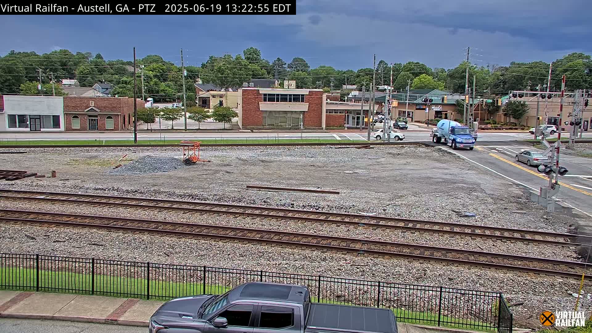 A mostly cloudy day reveals a view of railroad tracks, a construction site, and a street intersection with several vehicles, including a truck, in a small town.