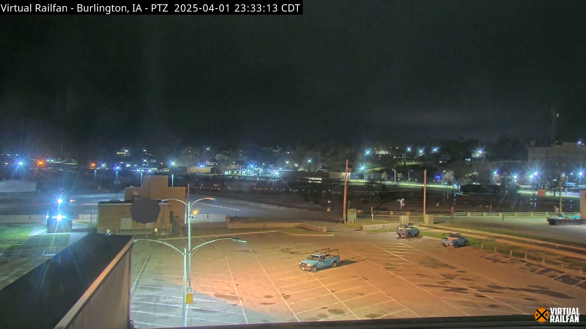 A nighttime view of a mostly empty parking lot with a few vehicles, overlooking a dimly lit town under a dark sky.