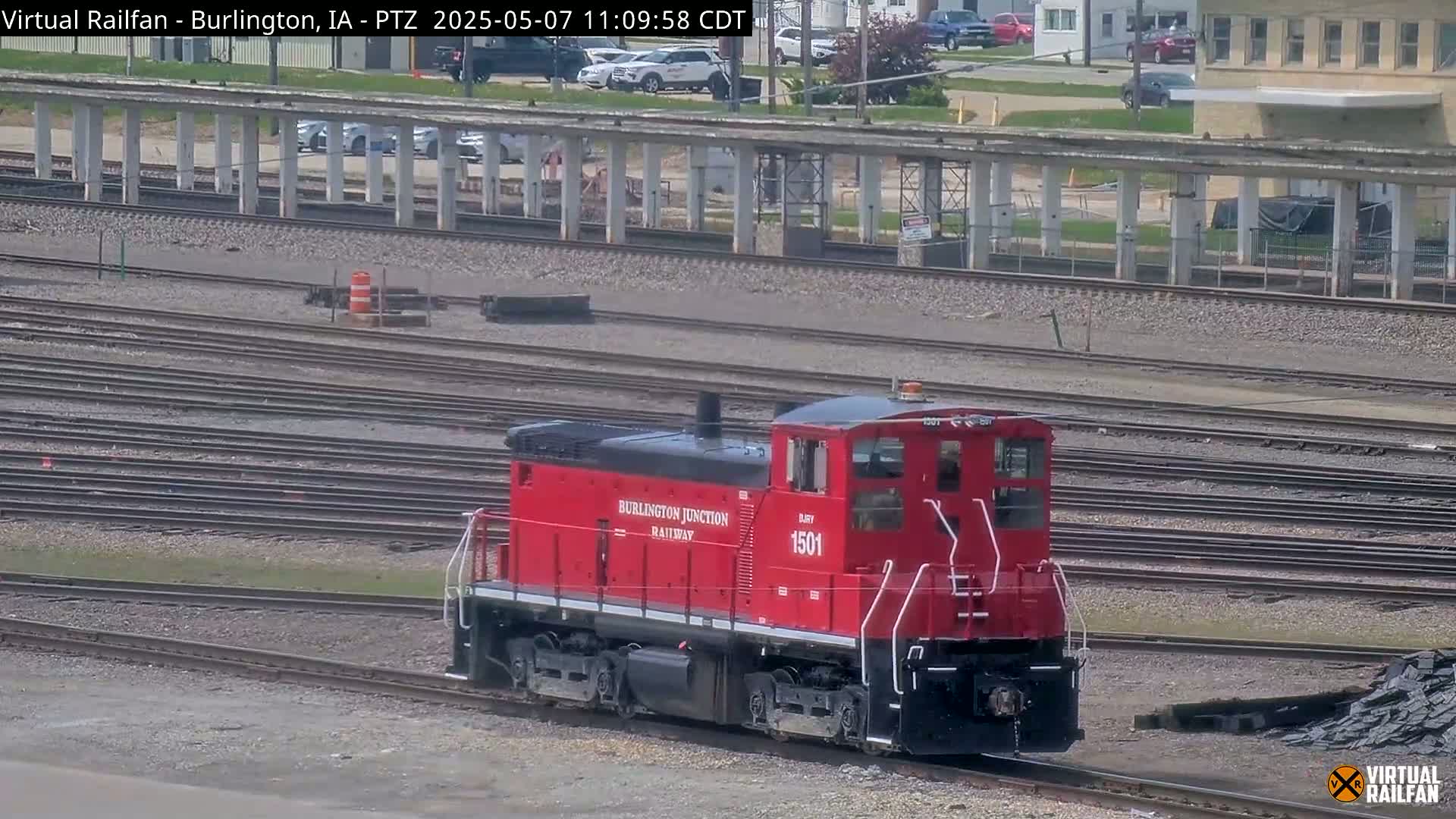 A red Burlington Junction Railway locomotive, numbered 1501, sits on a set of train tracks on a partly sunny day.