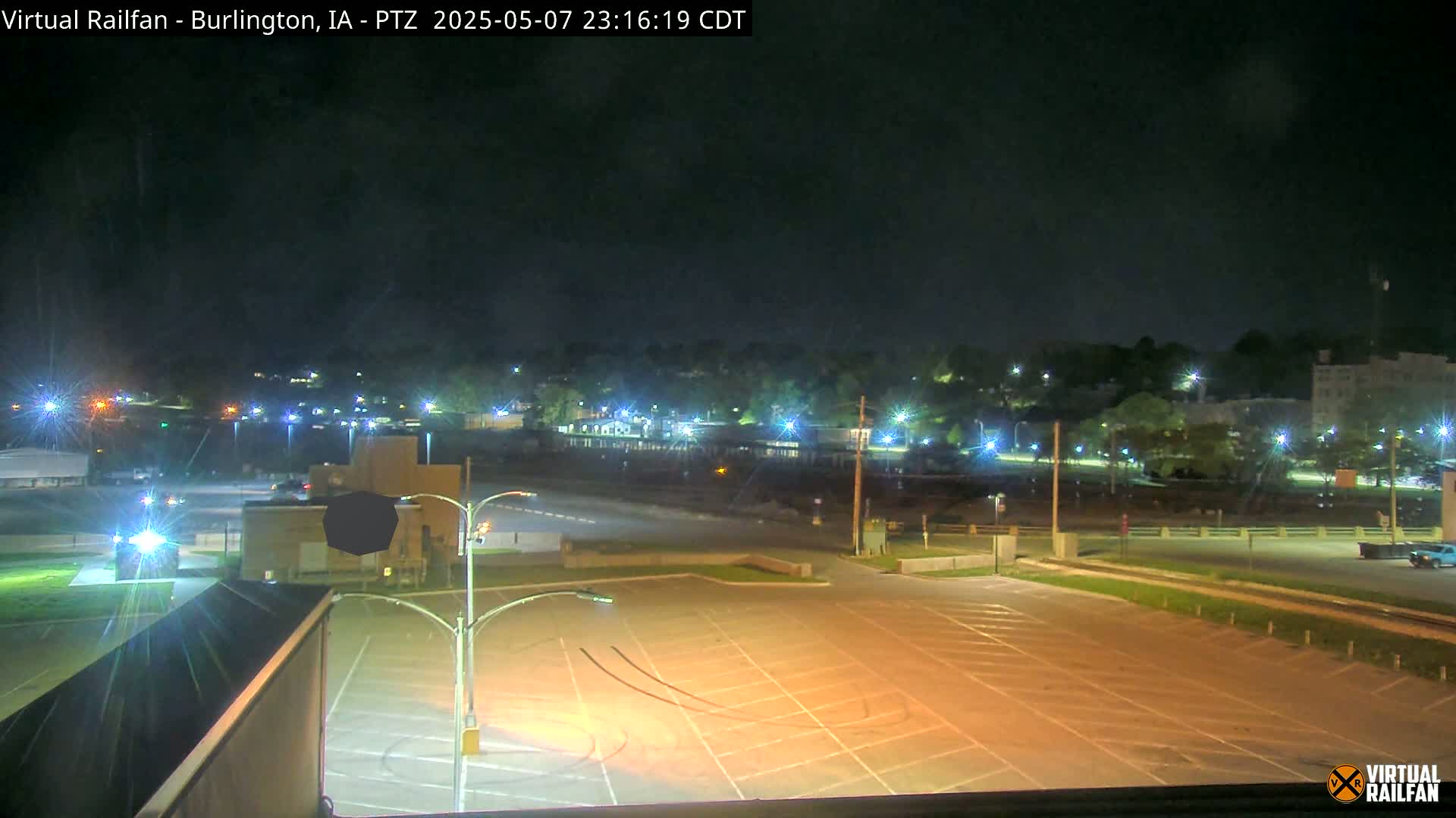A nighttime view of a mostly empty parking lot with a distant town illuminated by streetlights under a clear, dark sky.