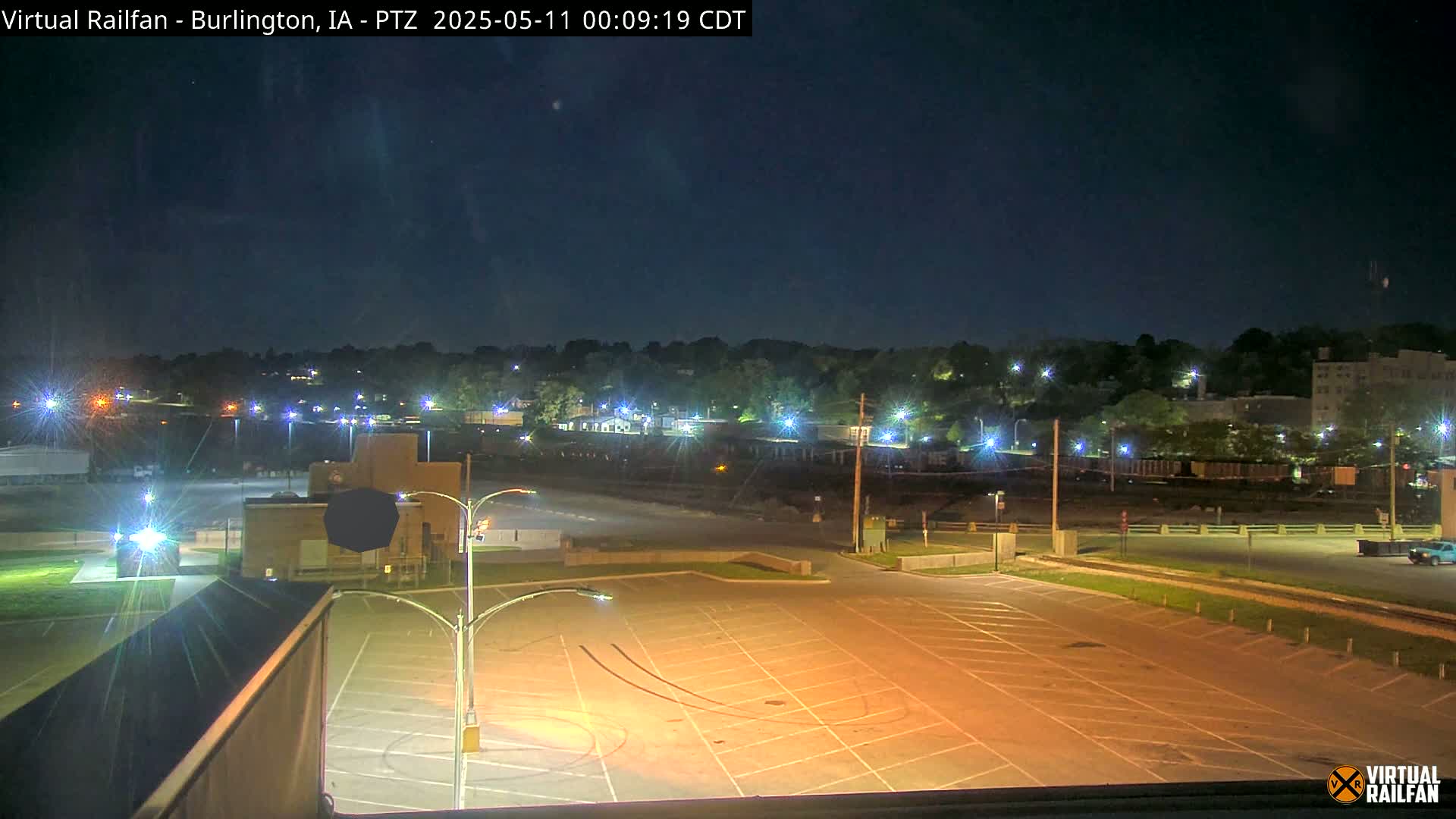 A nighttime view of a mostly empty parking lot with a distant cityscape illuminated by streetlights under a clear, dark sky.